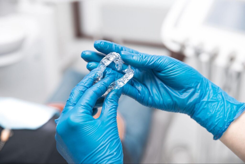 dentist holding Invisalign aligners in hand wearing blue gloves