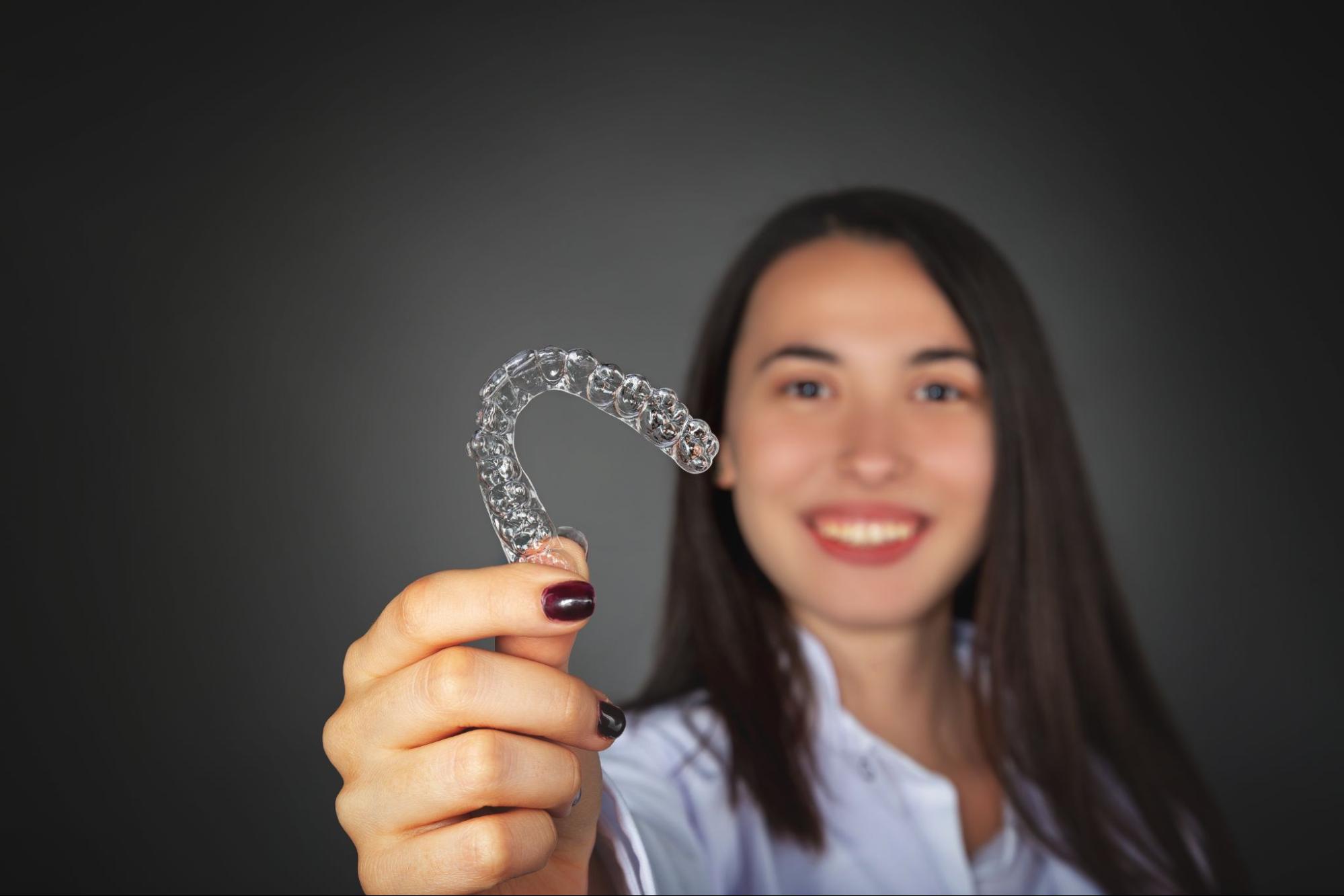 woman smiling at camera holding aligners