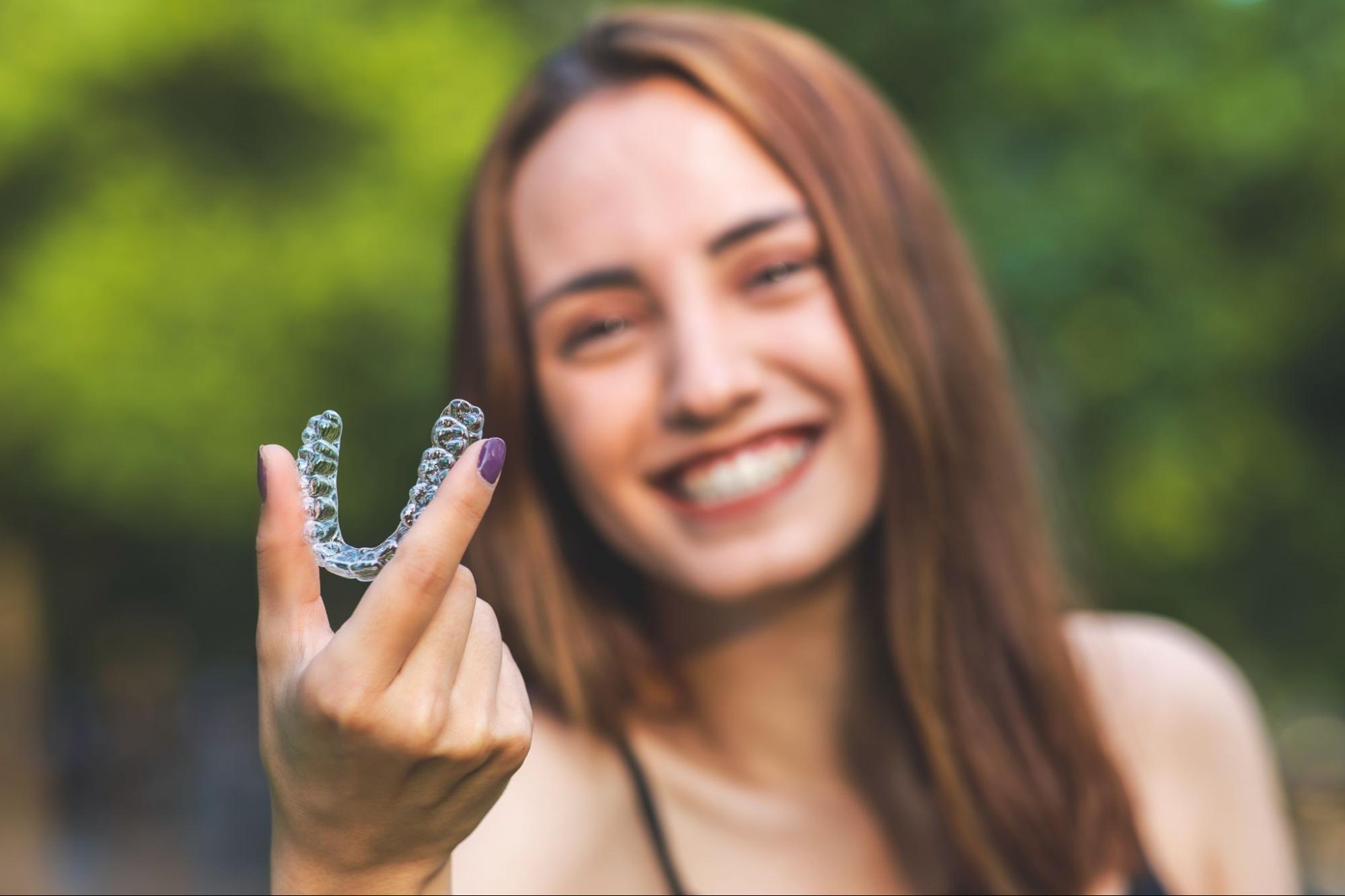 beautiful smiling turkish woman is holding an invisalign bracer with vibrant colours
