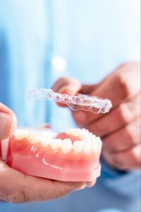 closeup the doctor puts transparent aligners on the teeth of the artificial jaw